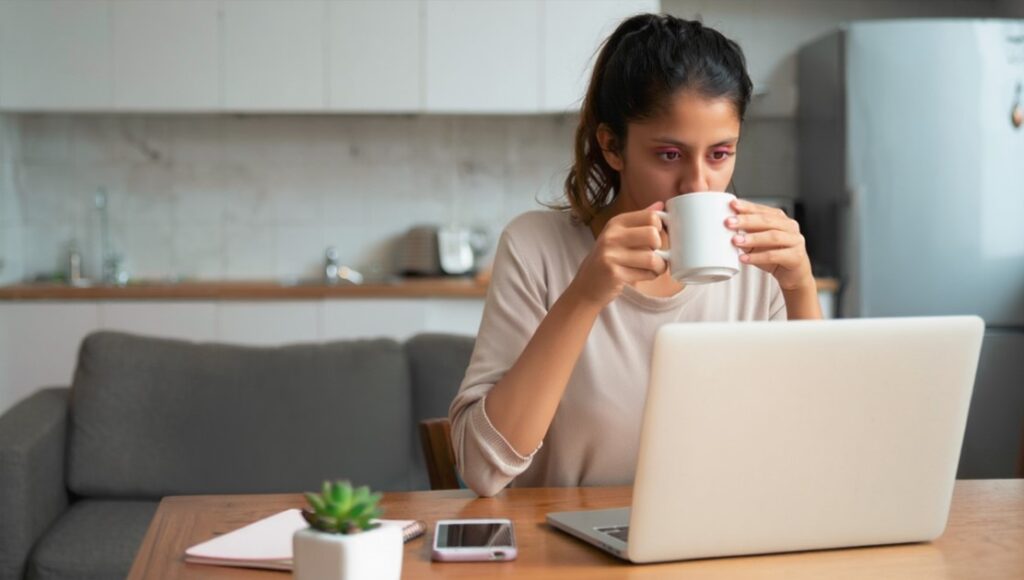 Mujer con ojos rojos frente a notebook en casa, síntoma relacionado con fatiga visual y espasmos oculares como el temblor de ojo.